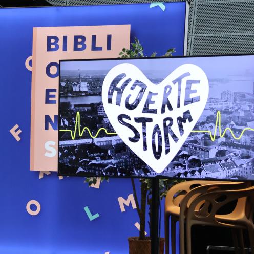 En stor skærm med en grafik på. Det er et hjerte foran Aalborgs Skyline. I hjertet står der Hjertestorm.